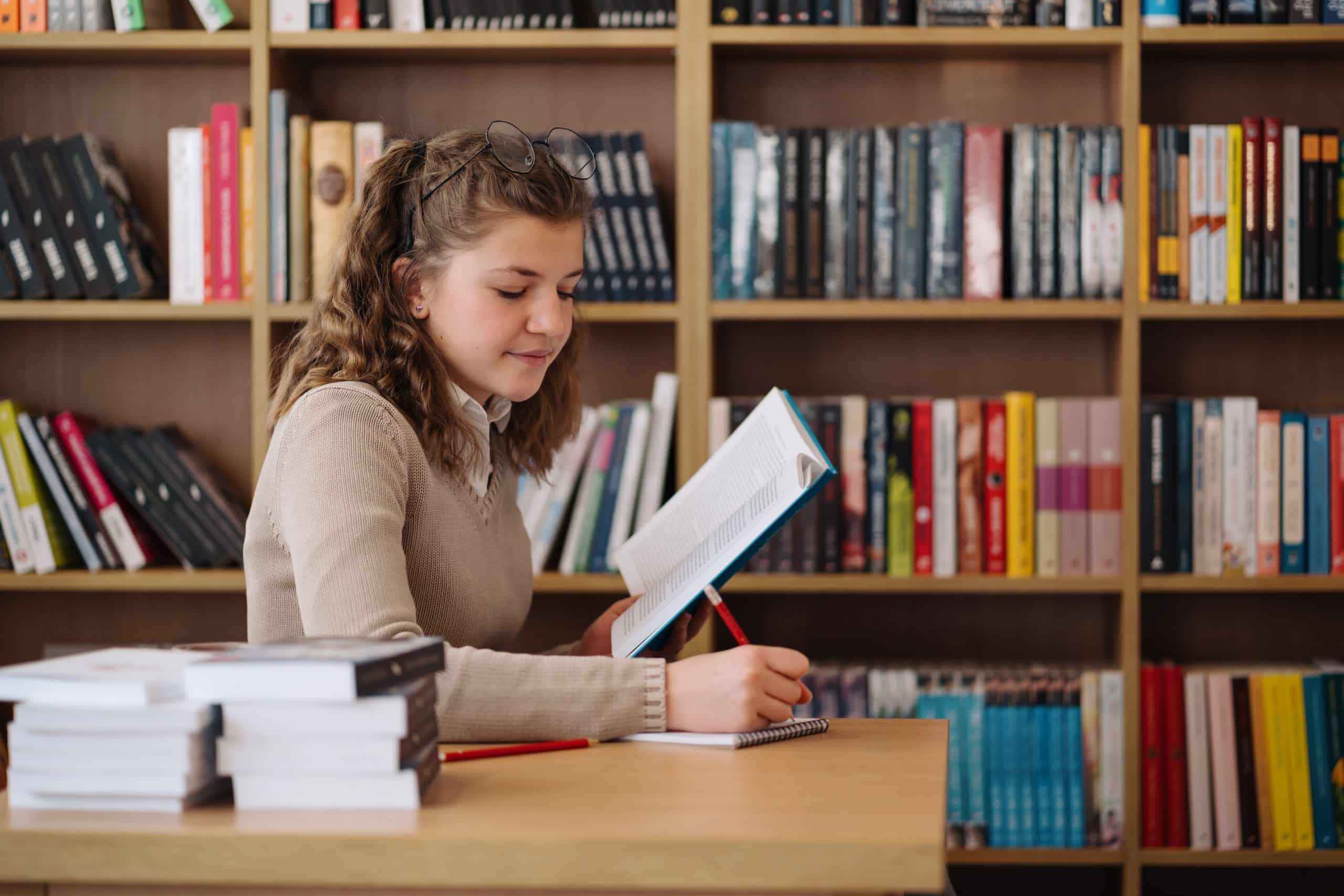 Studieboeken kopen door een studente die achter een bureau zit met daarachter een boekenkast.